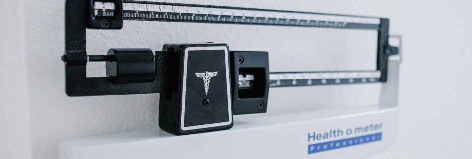 Medical balance scale with a ruler beam and a Healthometer label, featuring a caduceus symbol on the front panel