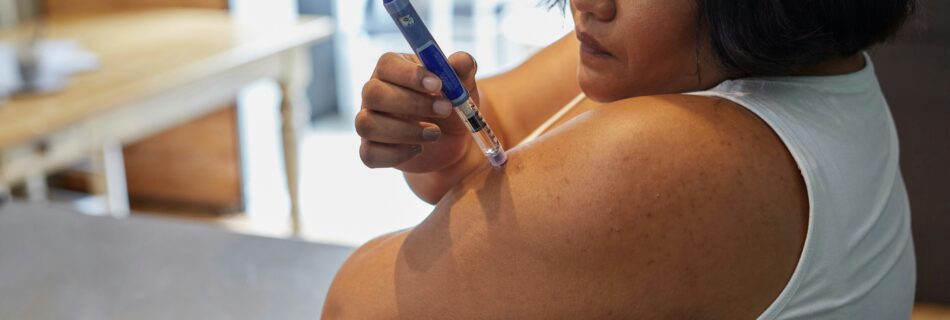 Woman receiving a vaccination in her upper arm using a syringe, close-up of the injector and her bare shoulder.